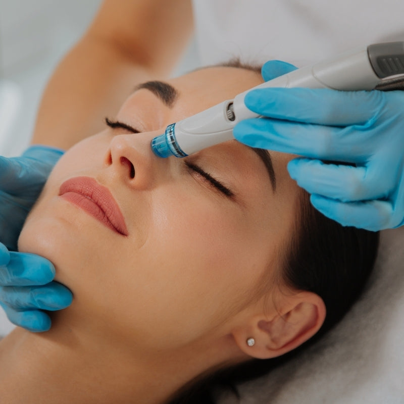Person receiving a hydrofacial treatment with a device held by gloved hands.